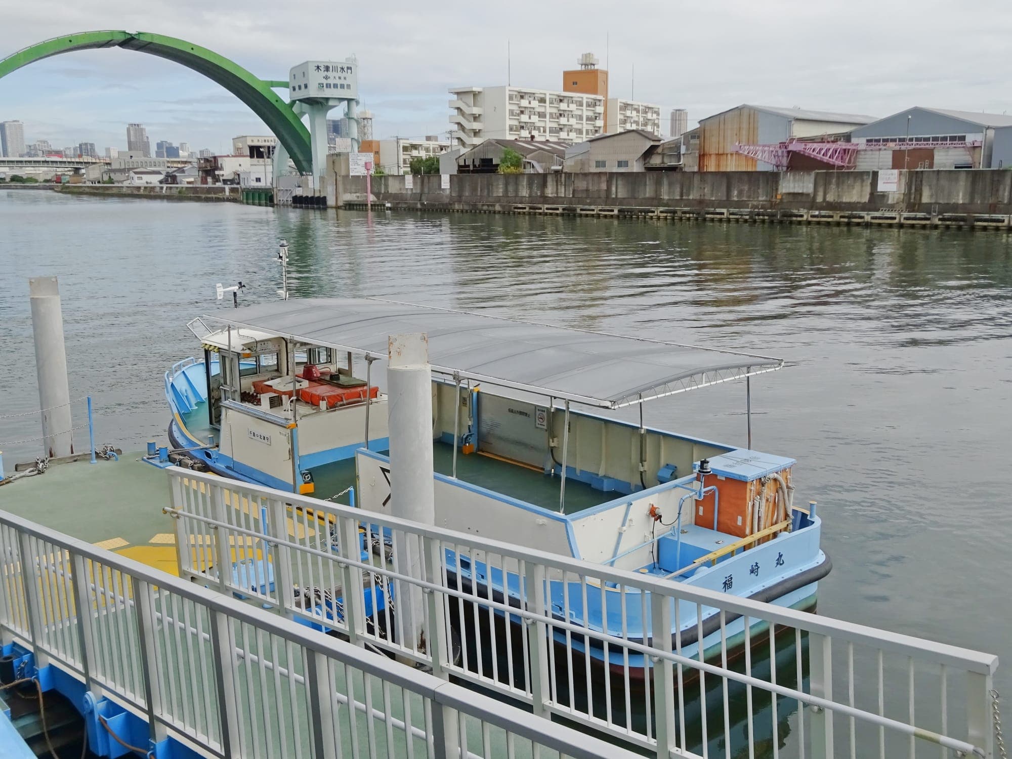 木津川を渡る市営渡船。後ろにアーチ形の水門