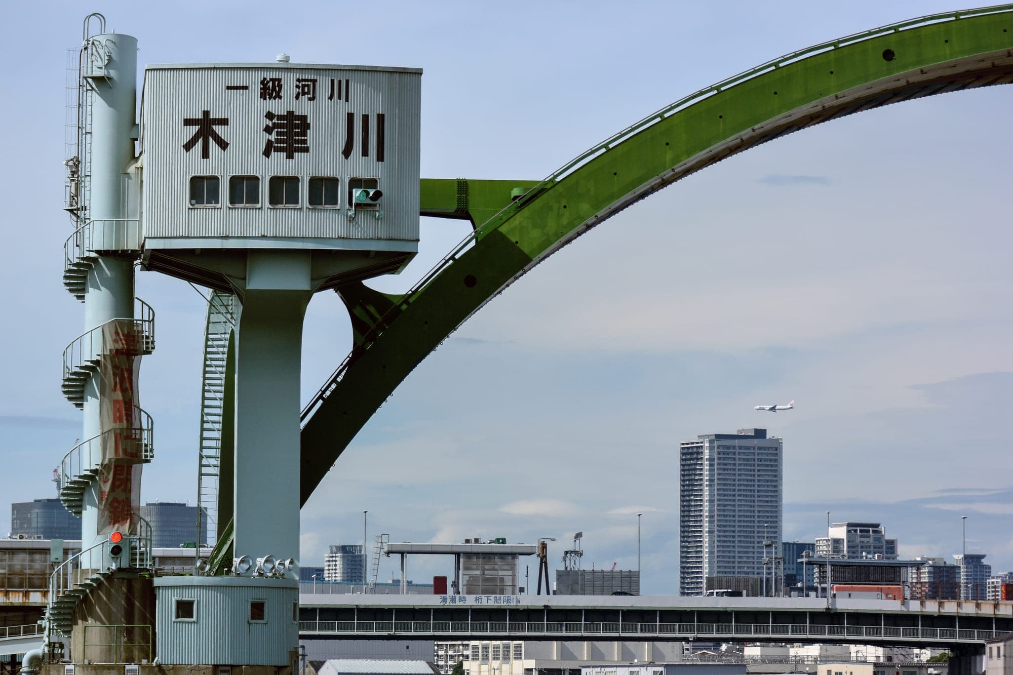 緑のアーチ形の木津川水門と、その向こうの街並み